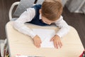 A cute first-grader boy in a school uniform at home while  at his desk makes a paper airplane during recess Royalty Free Stock Photo