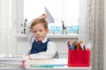 A cute first-grader boy in a school uniform at home while isolated at his desk makes a paper airplane during recess Royalty Free Stock Photo