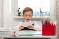 A cute first-grader boy in a school uniform at home while isolated at his desk makes a paper airplane during recess Royalty Free Stock Photo