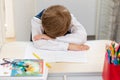 A cute first grader boy in a school uniform at home during a pandemic fell asleep doing homework at a desk with books and pencils.