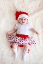 Cute five-month-old baby dressed in a santa hat and a red yuke lies on her back on a fluffy plaid. vertical photo Royalty Free Stock Photo