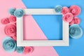 Cute flat lay with empty white picture frame surrounded by romantic paper craft roses on blue and pink background