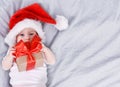 Cute four month old baby in a red Santa Claus hat lying on back holding gift