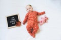 Four months old baby girl laying down on white background with letter board and teddy bear. Flat lay composition.