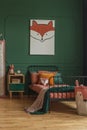 Cute fox hanging on a dark green wall in a child bedroom interior with metal bed, orange sheets and wooden bedside