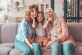 Cute franddaughter sitting on the couch with mother and grandmother and touching their faces with hands and looking at the camera