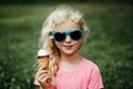 Cute funny adorable girl in sunglasses with dirty nose and moustaches eating ice cream from waffle cone. Happy cool hipster child Royalty Free Stock Photo