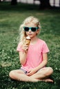 Cute funny adorable girl in sunglasses with dirty nose and moustaches eating ice cream from waffle cone. Happy cool hipster child Royalty Free Stock Photo