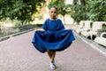 Cute and funny African baby girl wearing a colorful blue dress and smiling while standing in park alley background Royalty Free Stock Photo