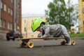 Funny baby in green helmet lying on belly on skateboard and pushing himself by one leg. Little skateboarder