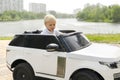 Cute funny blond little young toddler kid child boy sitting,driving,riding in electric toy car,automobile,jeep in park.Children Royalty Free Stock Photo