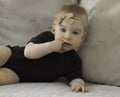 Cute funny caucasian blonde baby girl with brown bow,lying on sofa, looking at camera, putting fingers in mouth,looking Royalty Free Stock Photo