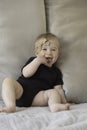 Cute funny caucasian blonde baby girl, sitting on background of beige sofa pillows in black body with brown bow,ribbon Royalty Free Stock Photo