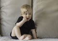 Cute funny caucasian blonde baby girl, sitting on background of beige sofa pillows in black body with brown bow,ribbon Royalty Free Stock Photo