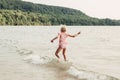 Cute funny Caucasian girl walking in lake river waves at sunset. Child jumping water on a beach. Authentic real lifestyle happy Royalty Free Stock Photo