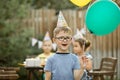 Cute funny four year old boy celebrating his birthday with family or friends in a backyard. Birthday party. Kid wearing party hat Royalty Free Stock Photo
