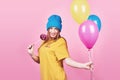 Cute funny girl in blue cap portrait holds an air colorful balloons and lollipop smiling on pink background. Beautiful Royalty Free Stock Photo