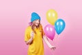 Cute funny girl in blue cap portrait holds an air colorful balloons and lollipop smiling on pink background. Beautiful Royalty Free Stock Photo