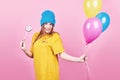 Cute funny girl in blue cap portrait holds an air colorful balloons and lollipop smiling on pink background. Beautiful Royalty Free Stock Photo