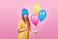 Cute funny girl in blue cap portrait holds an air colorful balloons and lollipop smiling on pink background. Beautiful Royalty Free Stock Photo