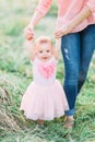 Cute funny happy baby girl making his first steps on a green grass, mother holding her hands supporting by learning to Royalty Free Stock Photo