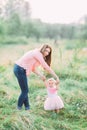 Cute funny happy baby girl making his first steps on a green grass, mother holding her hands supporting by learning to Royalty Free Stock Photo