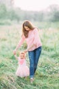 Cute funny happy baby girl making his first steps on a green grass, mother holding her hands supporting by learning to Royalty Free Stock Photo