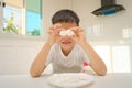 Cute funny little Asian boy sitting in the kitchen with a marshmallow at home, Unhealthy kids snacks Royalty Free Stock Photo