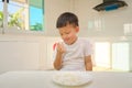 Cute funny little Asian boy sitting in the kitchen with a marshmallow at home, Unhealthy kids snacks Royalty Free Stock Photo