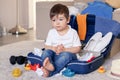 Cute funny little baby boy having rest siiting in blue suitcase tired of packing clothes and toys for vacation.