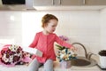 Cute funny little girl holding gift box sitting on kitchen table with bouquets of spring flowers and golden ballon 8 eight , Royalty Free Stock Photo