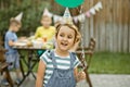 Cute funny six year old girl celebrating her birthday with family or friends in a backyard. Birthday party. Kid wearing party hat Royalty Free Stock Photo