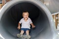 Cute funny smiling blonde little young toddler kid child boy going down pipe slide in playground. Children physical,emotional Royalty Free Stock Photo