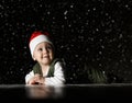 Happy infant boy toddler in red Santa hat and white - green clothes is lying on floor looking at upper corner under snow Royalty Free Stock Photo