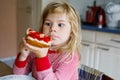 Cute funny toddler girl eats sweet bun for breakfast. Happy child eating bread roll with strawberry jam. Health food for Royalty Free Stock Photo