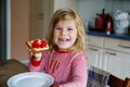 Cute funny toddler girl eats sweet bun for breakfast. Happy child eating bread roll with strawberry jam. Health food for Royalty Free Stock Photo