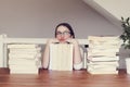 Cute funny tween girl in glasses sitting a table with pile of books looking sceptically and daydreaming of holidays. Royalty Free Stock Photo