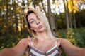 Cute funny young woman blonde in a vintage pink striped dress resting in the forest on a sunny day and taking pictures of herself Royalty Free Stock Photo