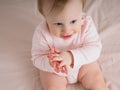 Cute gentle baby girl, 10 months old, sitting on the bed, clapping her hands, smiling, close-up. Portrait of a girl in pink tones Royalty Free Stock Photo