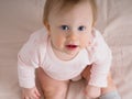 Cute gentle baby girl, 10 months old, sitting on the bed, looking closely at the camera, close-up, high angle view. Portrait of a Royalty Free Stock Photo