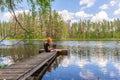 Cute ginger girl sitting on wooden planked footway and working with laptop in summer day against beautiful landscape of northern Royalty Free Stock Photo