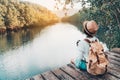 girl backpacking and sitting on the wood plank resting and looking on the river