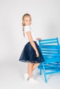 Cute girl with blond curly hair in school fashion clothes with blue chair