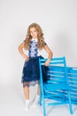 Cute girl with blond curly hair in school fashion clothes with blue chair