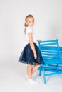 Cute girl with blond curly hair in school fashion clothes with blue chair