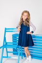 Cute girl with blond curly hair in school fashion clothes with blue chair