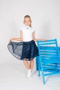 Cute girl with blond curly hair in school fashion clothes with blue chair