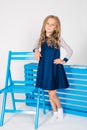 Cute girl with blond curly hair in school fashion clothes with blue chair