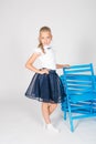 Cute girl with blond curly hair in school fashion clothes with blue chair