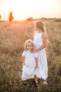 Cute girl with blond long hair with a younger sister in a summer field at sunset